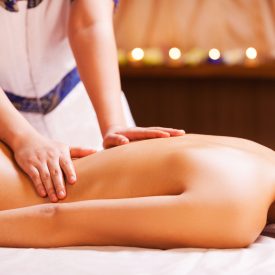 Massaging stress away. Close-up of young shirtless woman lying on front while massage therapist massaging her back